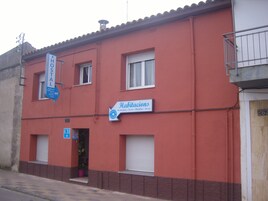 Un edificio de fachada roja, con un letrero que dice 'Habitaciones' e indicando las habitaciones, y un letrero de 'Hostal' sobre la entrada.