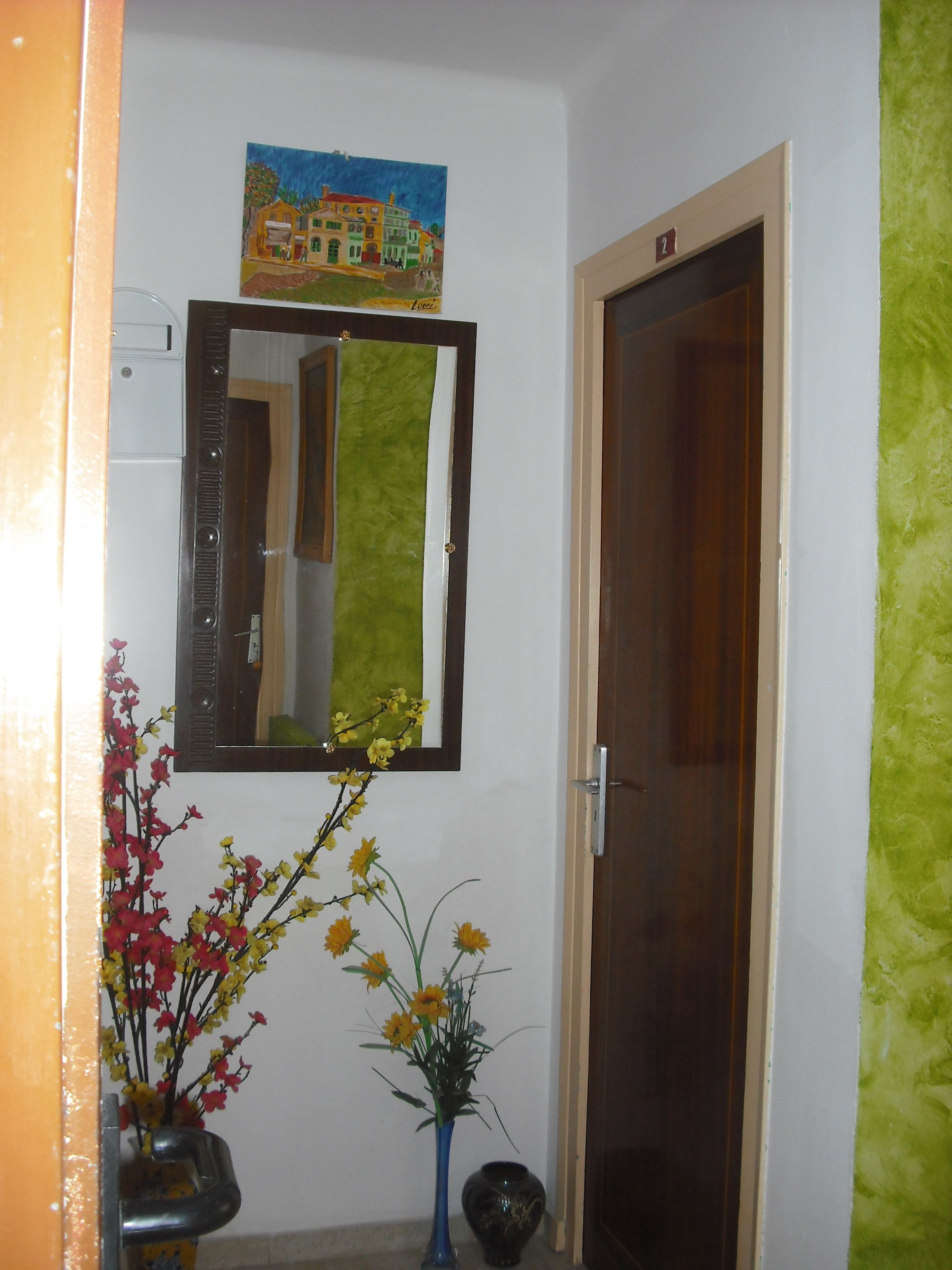 A hallway with a mirror, a painting, a vase with flowers, and a door.