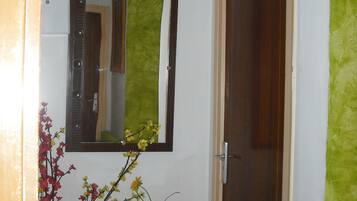 A hallway with a mirror, a painting, a vase with flowers, and a door.