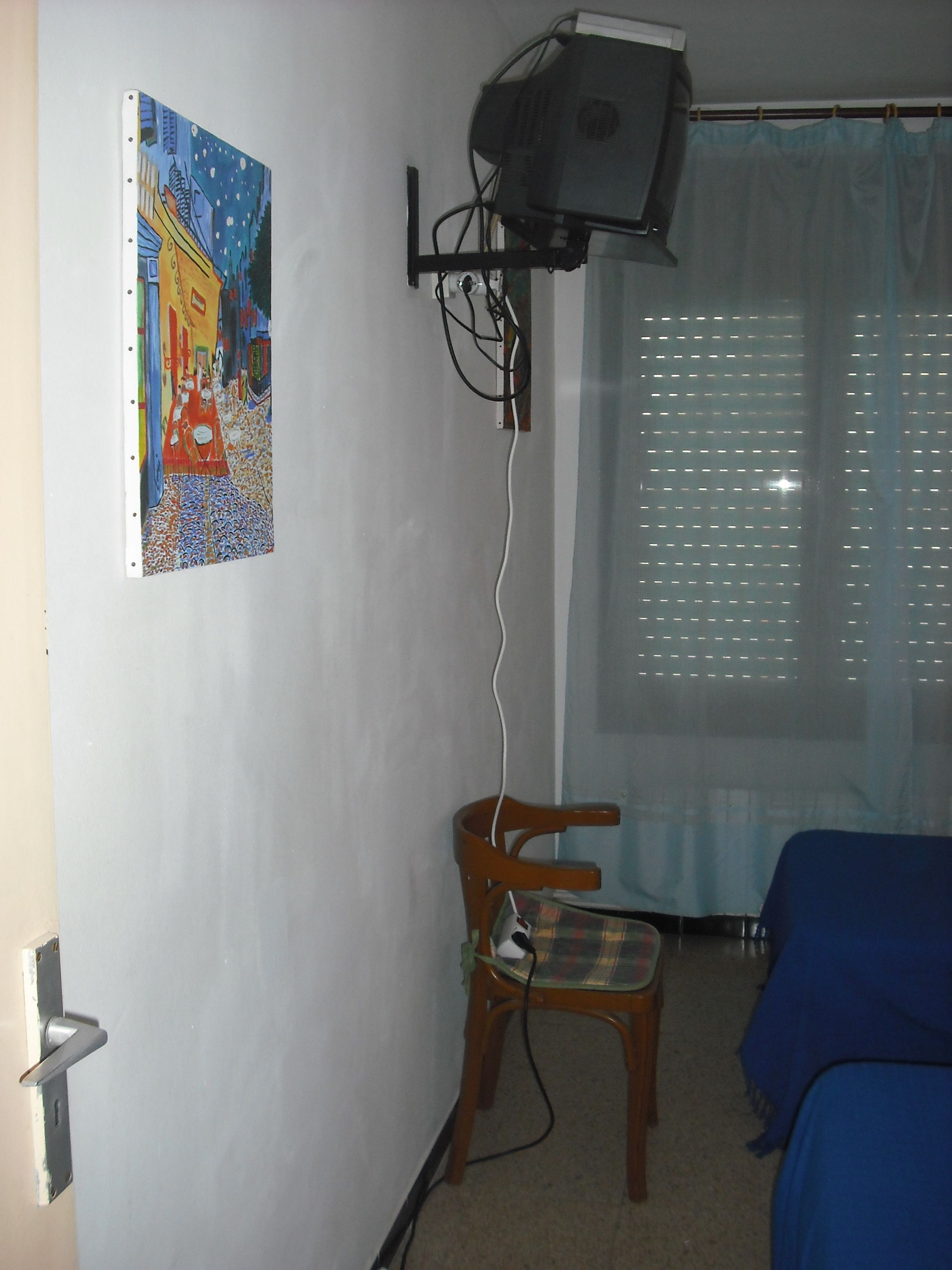 A room with a bed, a chair, a wall-mounted projector, and a painting.