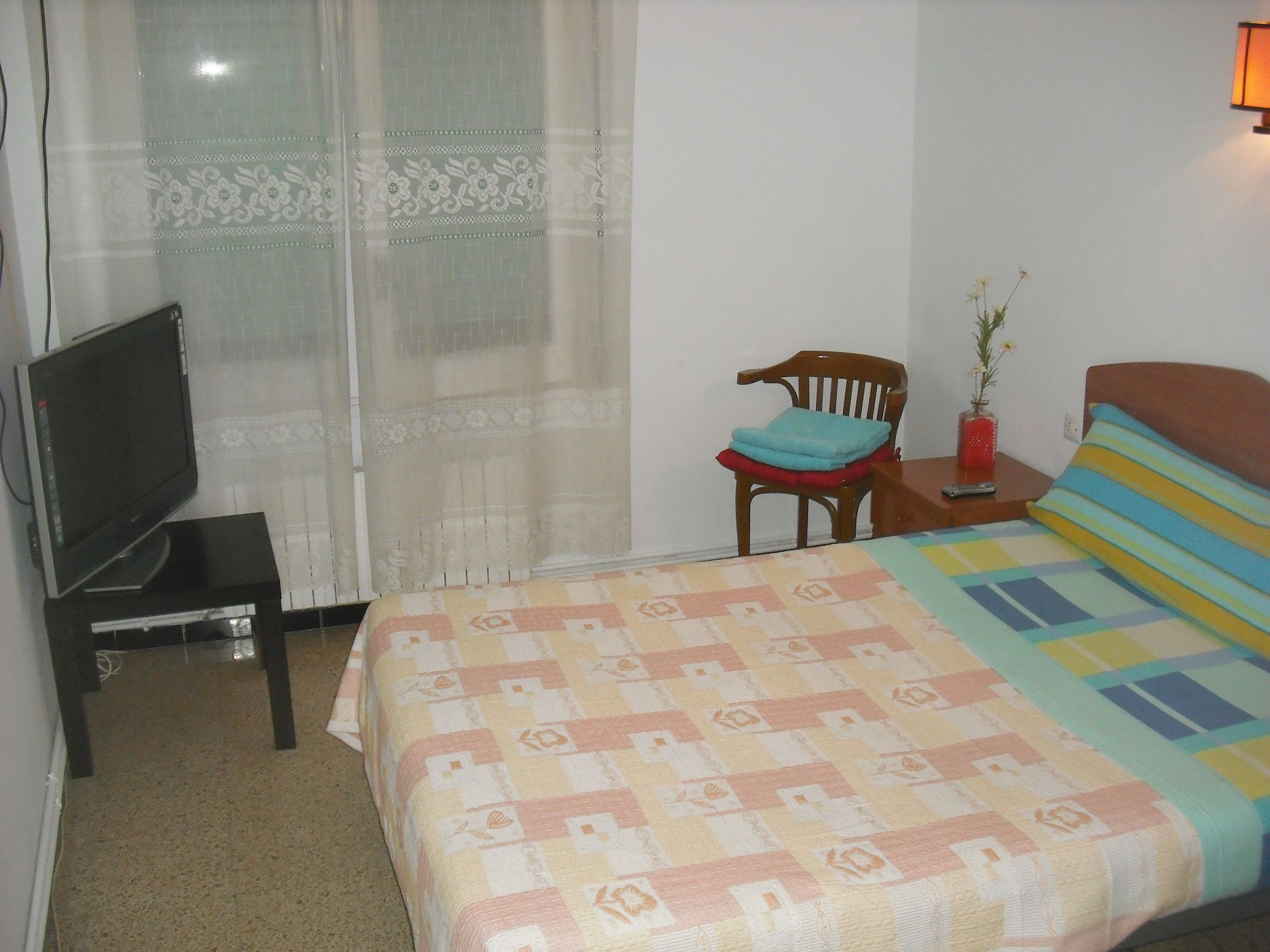 A hotel room with a bed, a chair, a small table, a television, and a window with curtains.