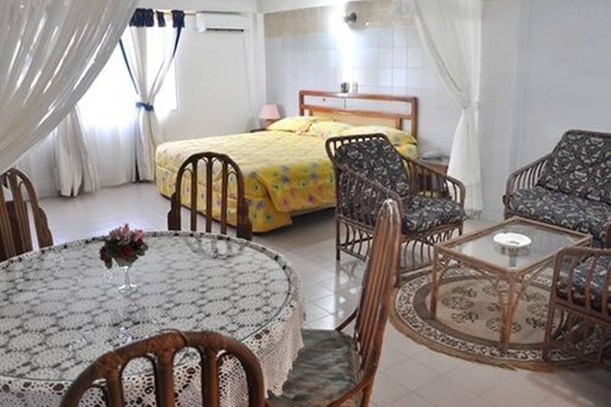 A hotel room with a bed, two chairs, a round table, and a window with curtains.