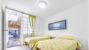 A room with two beds, a painting on the wall, and a view of a pool area through the door. - Hotel Santa Barbara (Villavicencio)