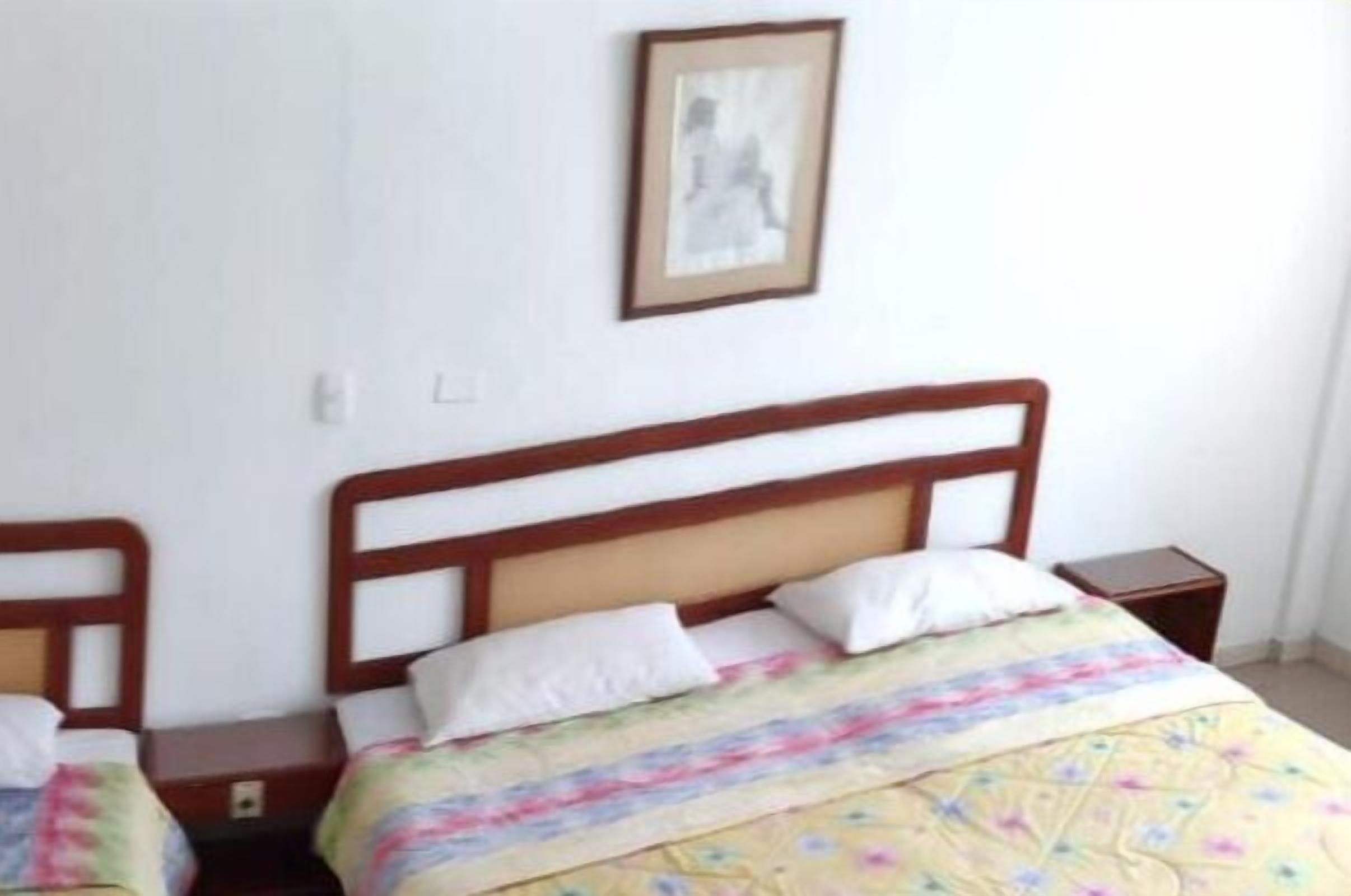 Una cama individual con cabecera de madera, una colcha floral colorida y una mesita de noche pequeña.