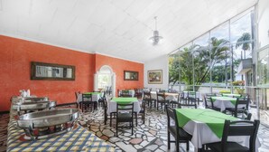 A restaurant with tables covered in green tablecloths, stone flooring, and orange walls. - Hotel Santa Barbara (Villavicencio)