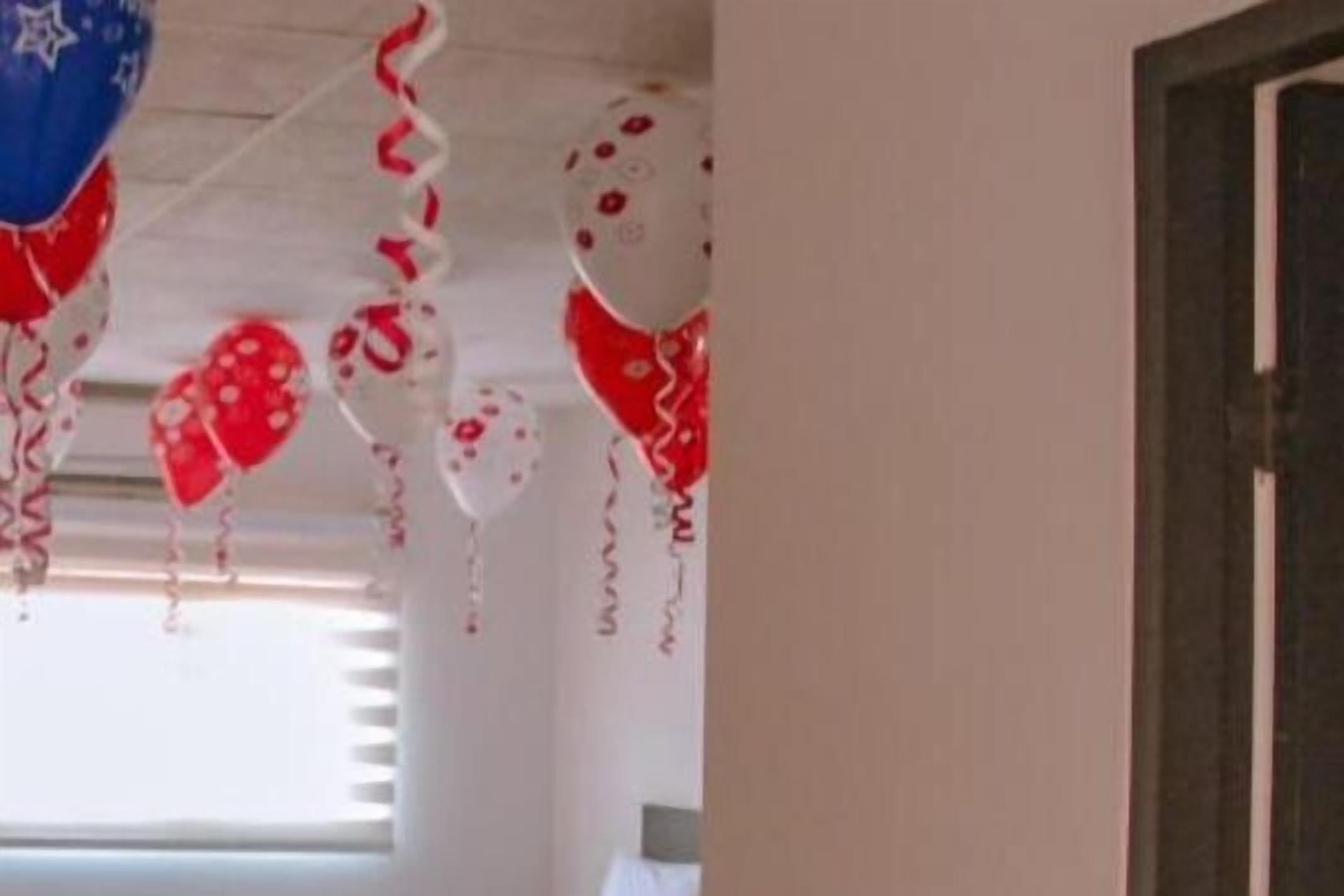 Una habitación con techo blanco, globos rojos y blancos, y una ventana con persianas.
