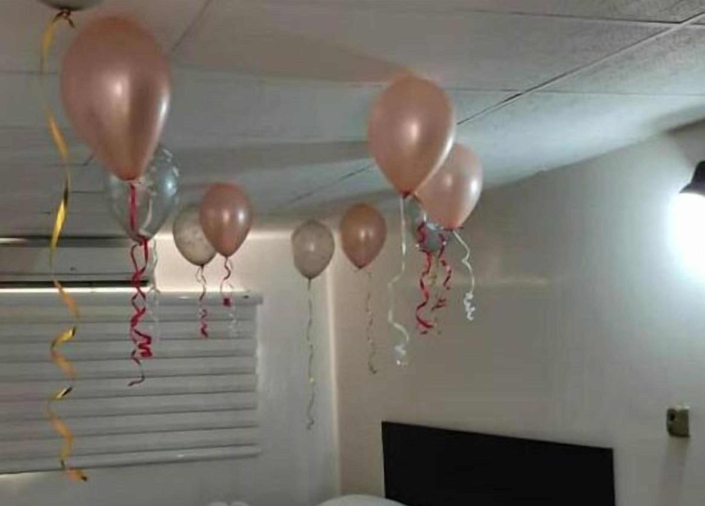 A room with a bed, a window with blinds, and balloons hanging from the ceiling.