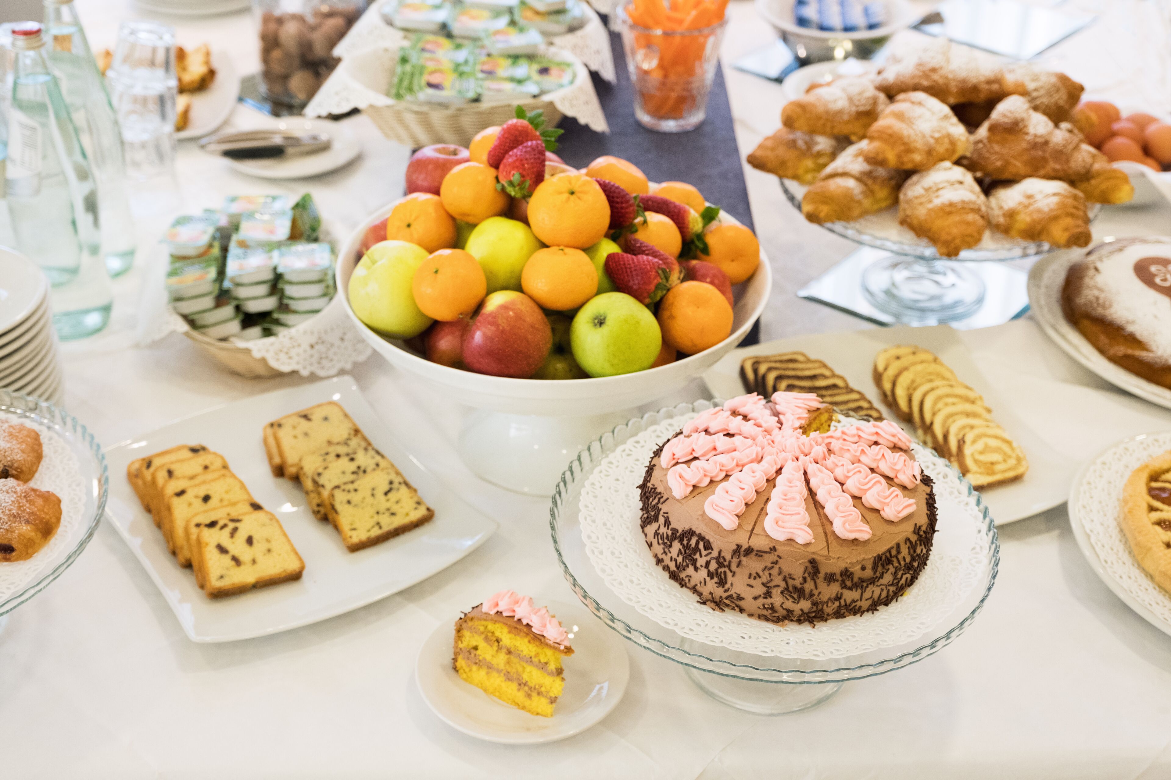 A buffet table with various food items including fruits, pastries, and desserts.