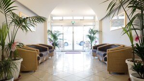A lobby with a tiled floor, wicker furniture, and potted plants. - St. Pierre (Rimini)