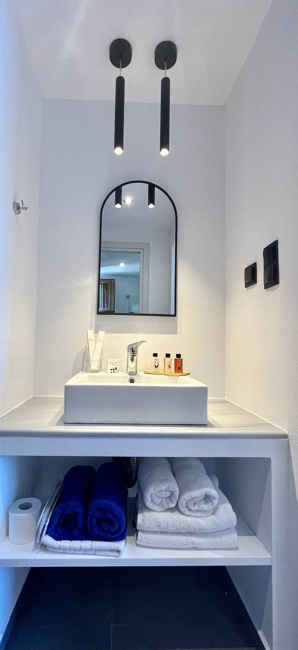 Ein modernes Badezimmer mit einem weißen Waschbecken, einem Spiegel und Ablagefläche für Handtücher.