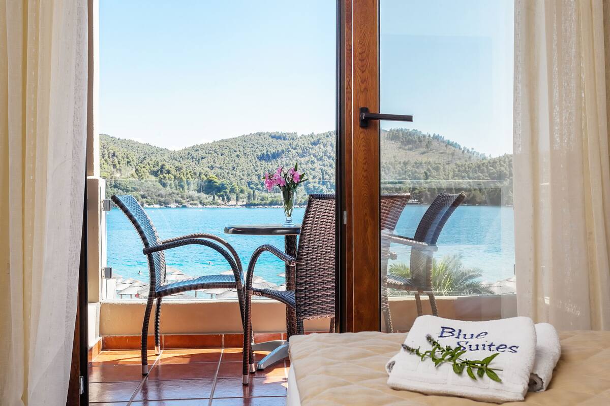 A balcony with wicker chairs, a table with a vase of flowers, and a bed with a towel labeled "Blue Suites".