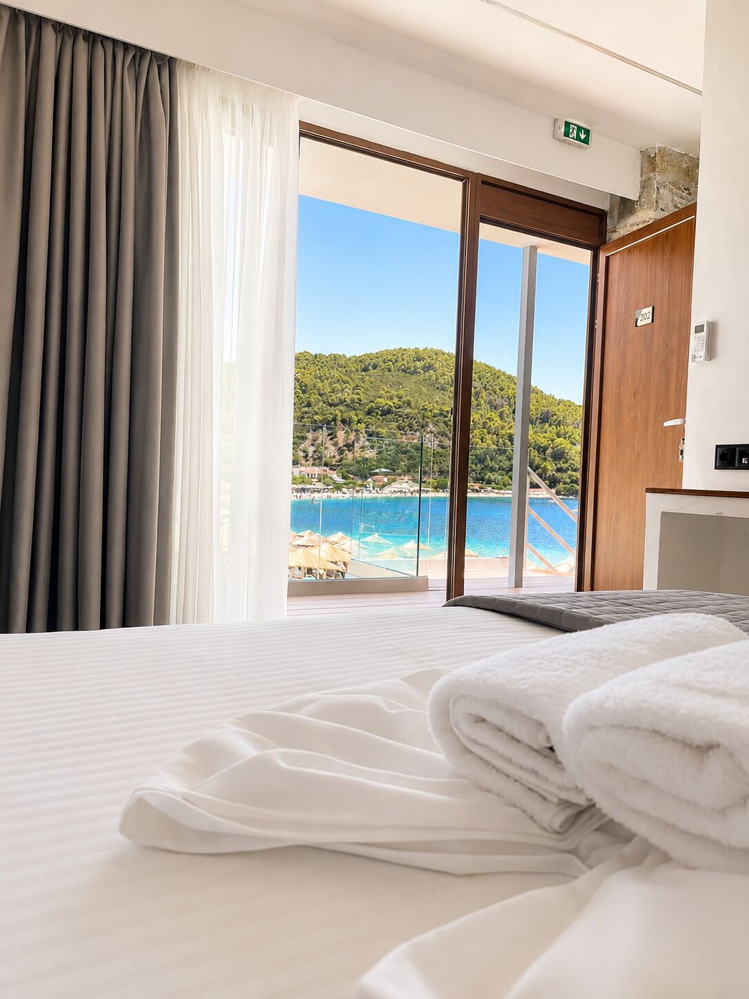 Une chambre d’hôtel avec un lit, une vue sur la plage et une porte donnant sur l’extérieur.