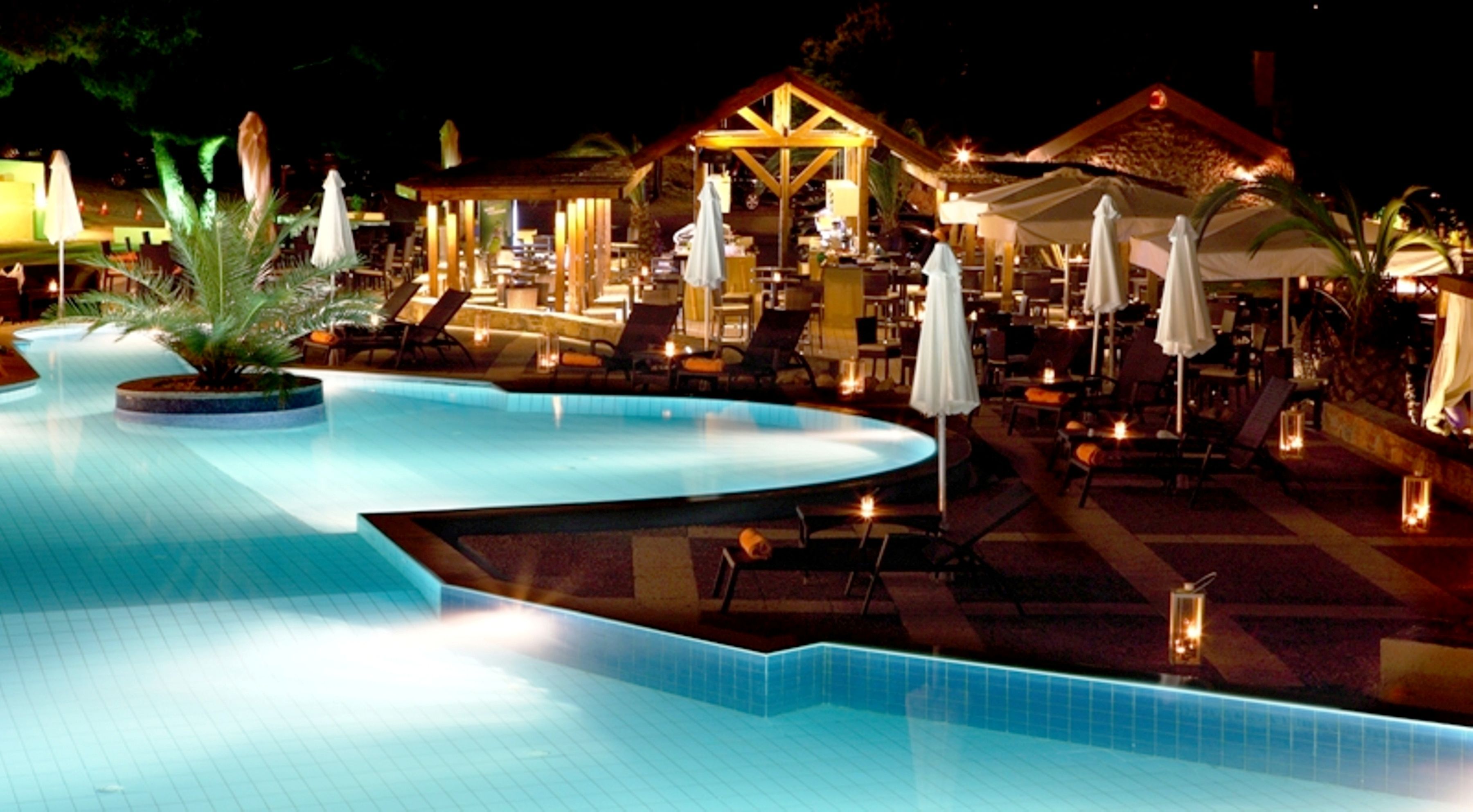 A nighttime pool area with lounge chairs, umbrellas, and a wooden gazebo.