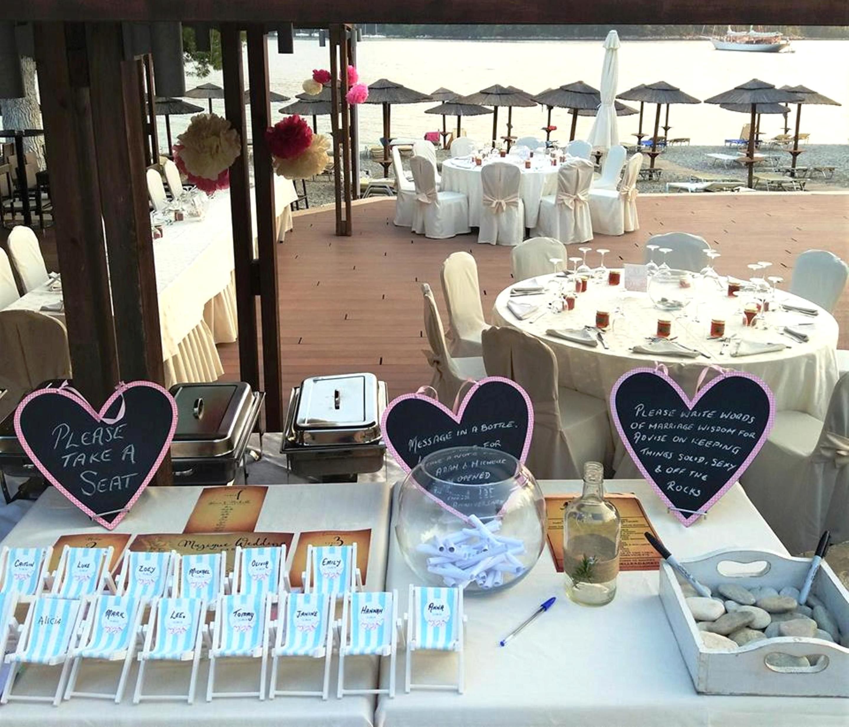 An outdoor wedding setup with round tables, chairs, and a view of the beach.