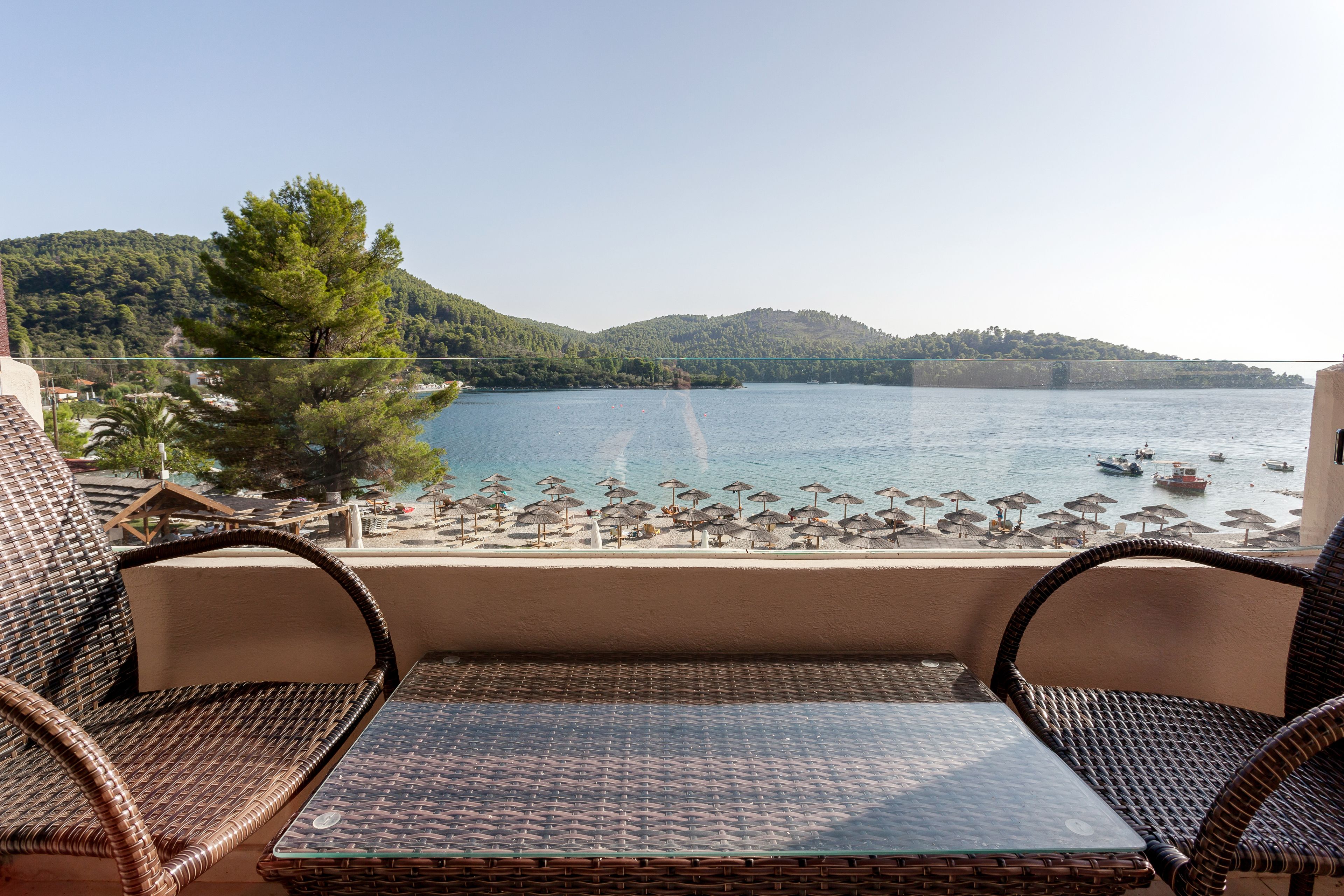 Una terraza con mobiliario de mimbre que da a una playa con sombrillas y barcos.