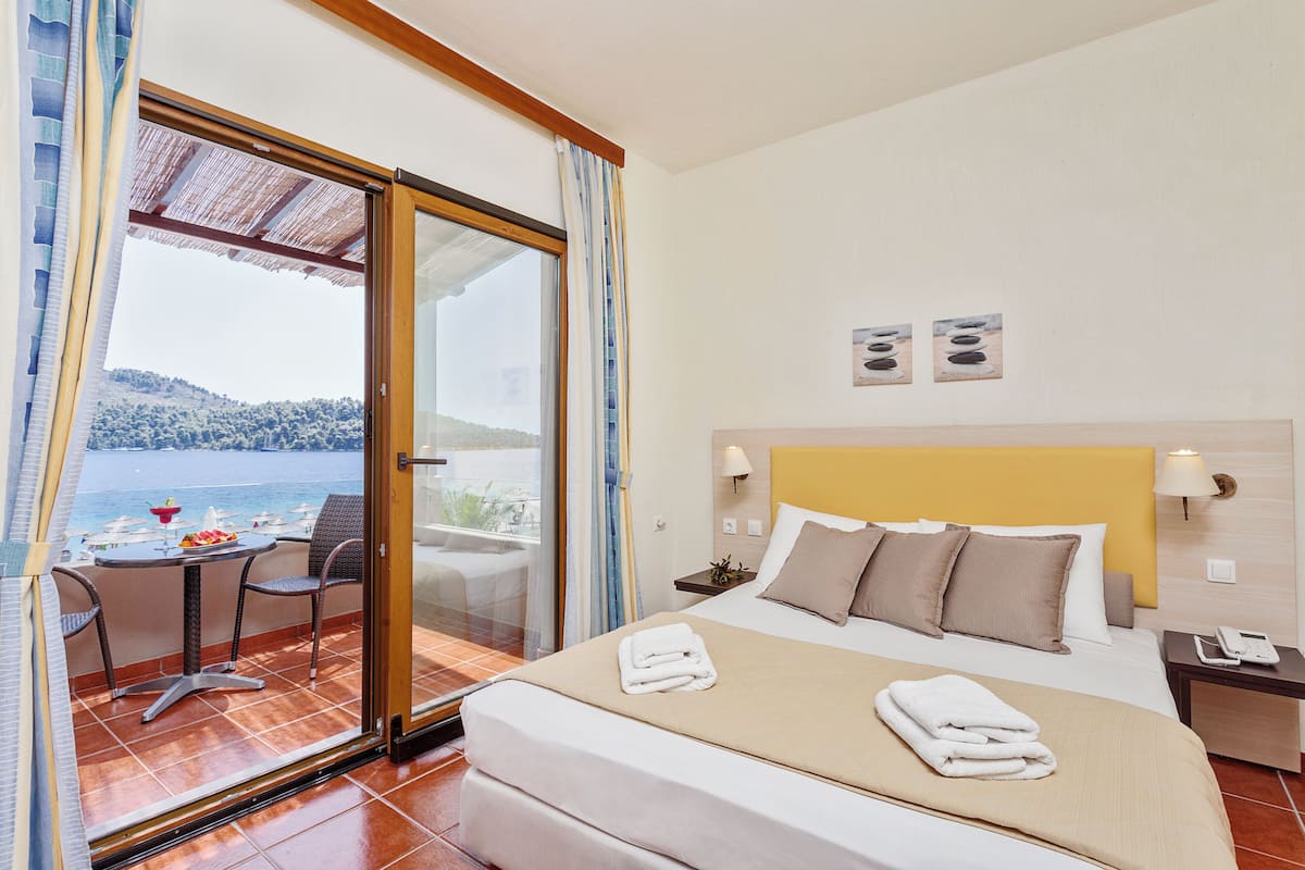 Une chambre d’hôtel avec un lit, une petite table et des chaises, une vue sur la mer et un balcon avec une table et des chaises.