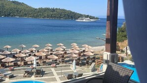 Un balcón con vista a una playa, una piscina y un yate a lo lejos.