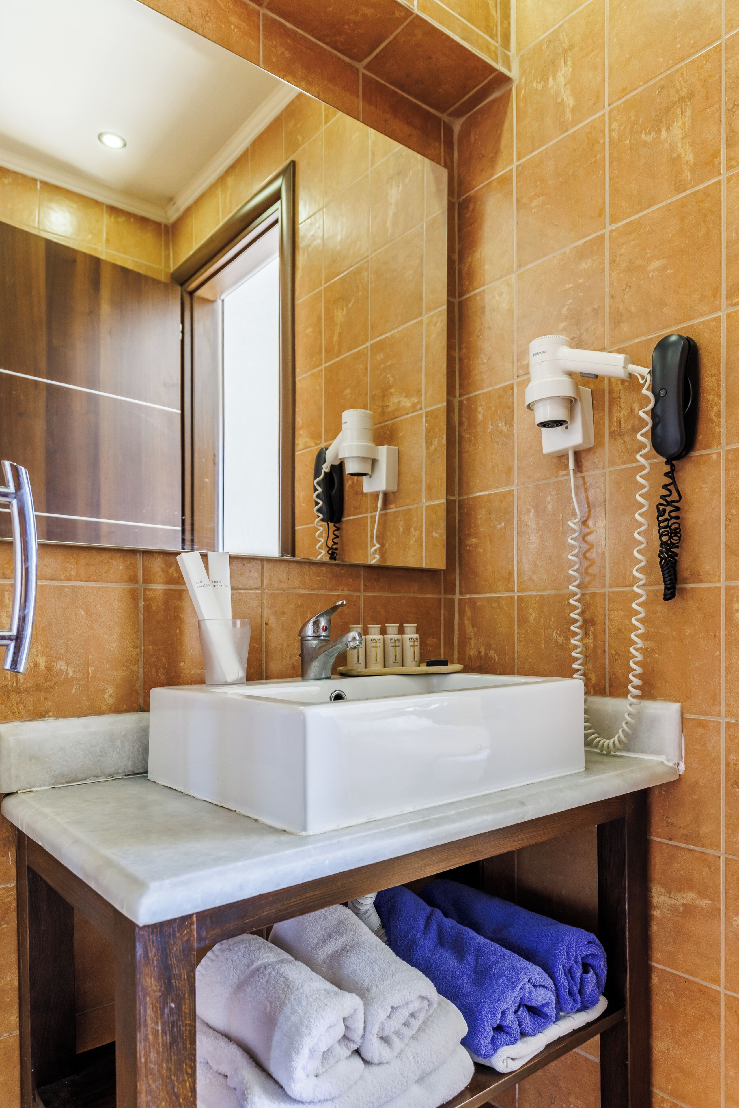 A bathroom with a white sink, a mirror, a hairdryer, and a towel rack with towels.