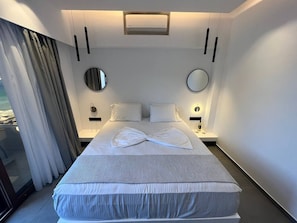 Ein modernes Hotelzimmer mit einem großen Bett, zwei Nachttischen, einem runden Spiegel und Meerblick.