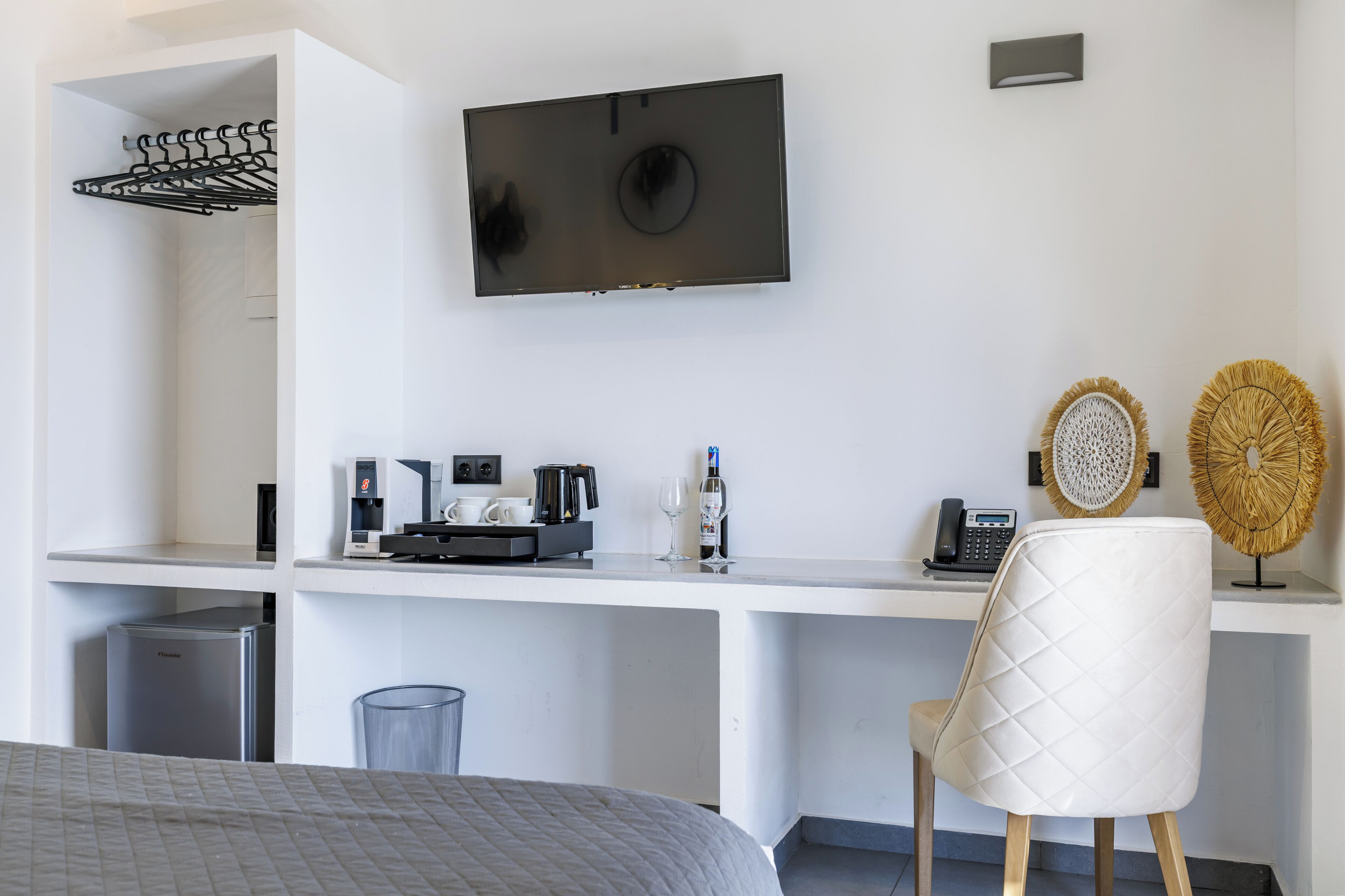 Ett modernt hotellrum med en säng, ett skrivbord med en kaffemaskin, en TV och dekorativa föremål.