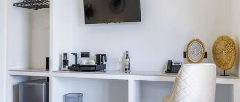 Ett modernt hotellrum med en säng, ett skrivbord med en kaffemaskin, en TV och dekorativa föremål.