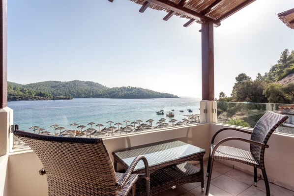A balcony with wicker furniture, a glass table, and a view of the sea and hills. - Blue Green Bay (Skopelos)