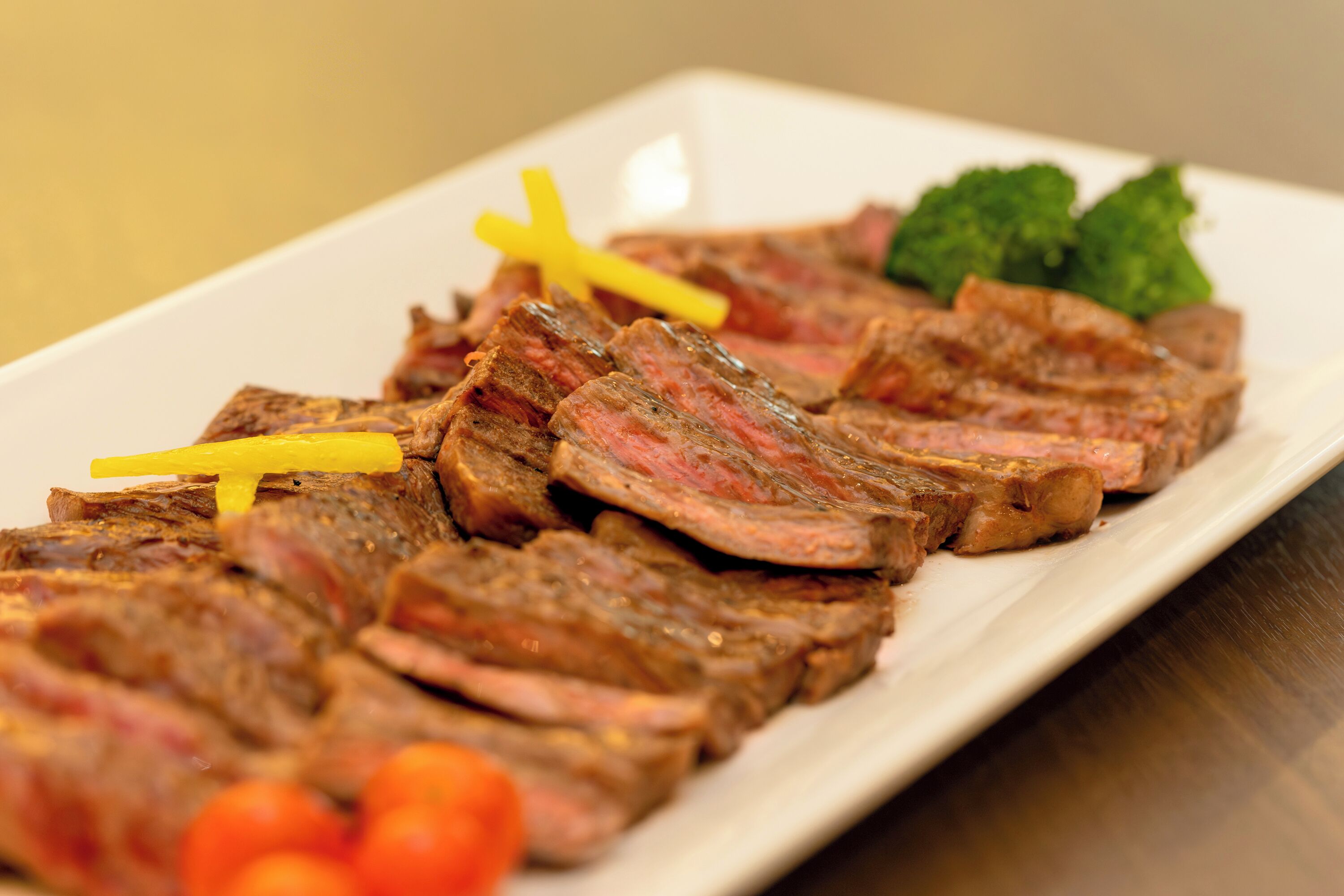 A white rectangular plate with sliced meat, garnished with green leaves and yellow sticks.