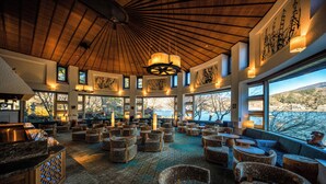 A spacious lounge with multiple seating areas, large windows offering views of the outdoors, and a wooden ceiling. - Fuji Lake Hotel (Fujikawaguchiko)