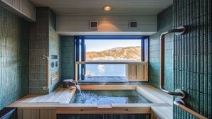 A hot tub with a view of a body of water and hills, surrounded by tiled walls and wooden flooring. - Fuji Lake Hotel (Fujikawaguchiko)