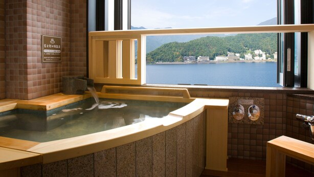 A hot tub with a view of a lake and buildings in the distance. - Fuji Lake Hotel (Fujikawaguchiko)