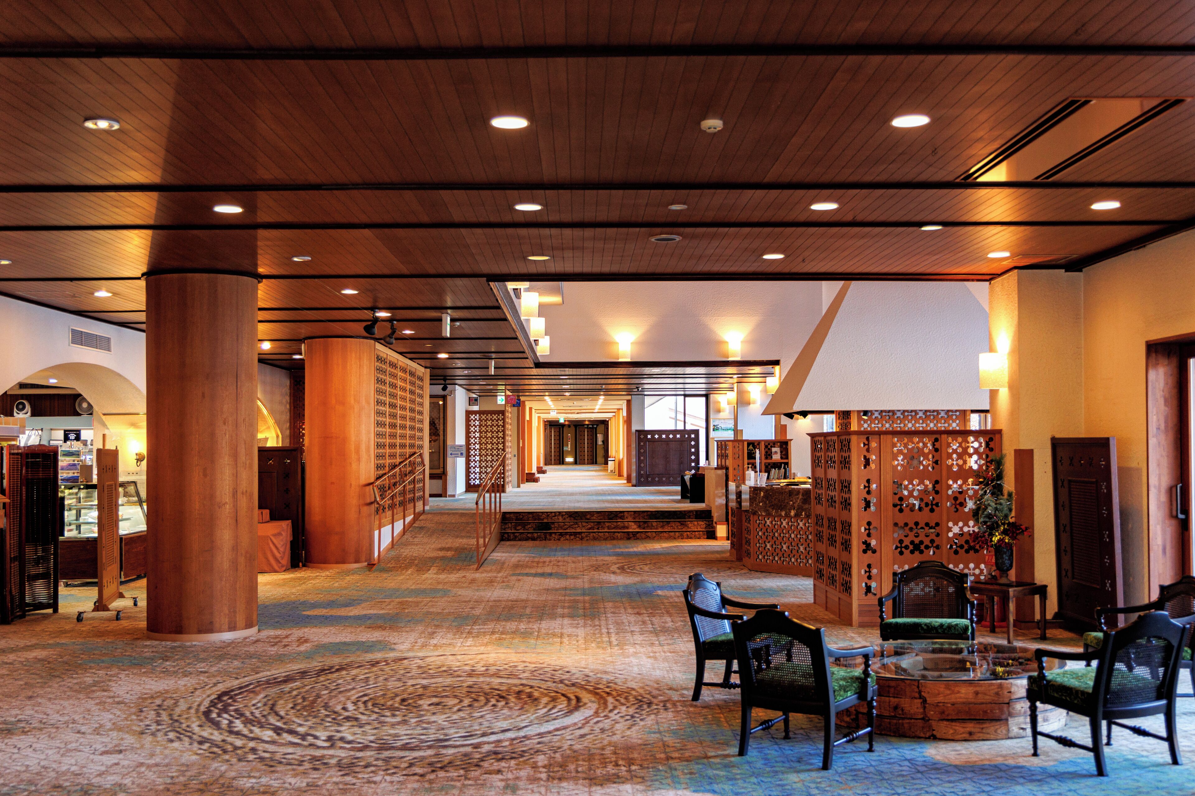 A spacious lobby with wooden flooring, a central staircase, and seating areas.
