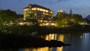 A multi-story hotel with balconies, a lake in the foreground, and a mountain in the background. - Fuji Lake Hotel (Fujikawaguchiko)