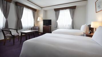 A hotel room with two beds, a desk, a chair, a television, and a lamp.