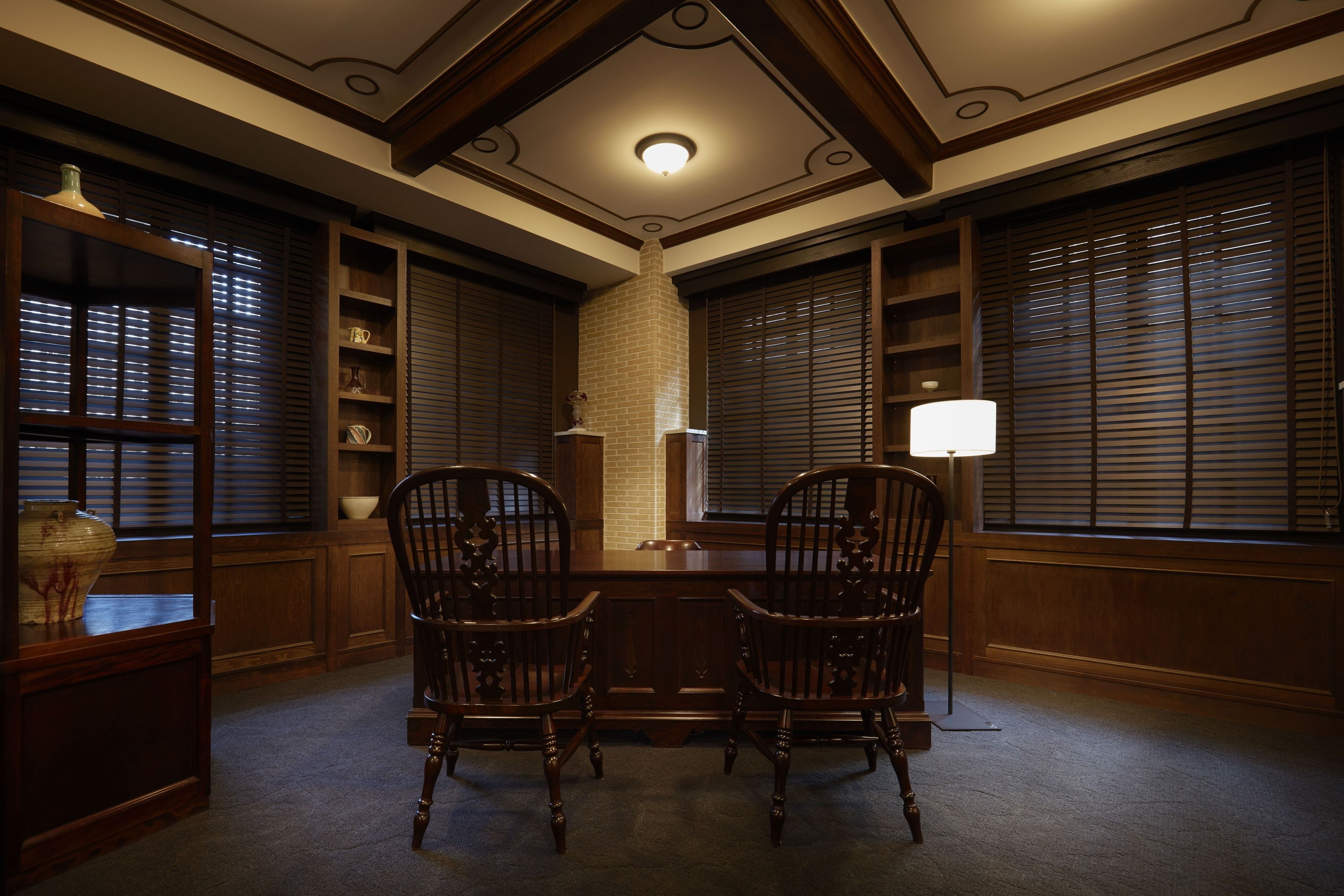 A dining area with a wooden table, two chairs, a vase, and a lamp.
