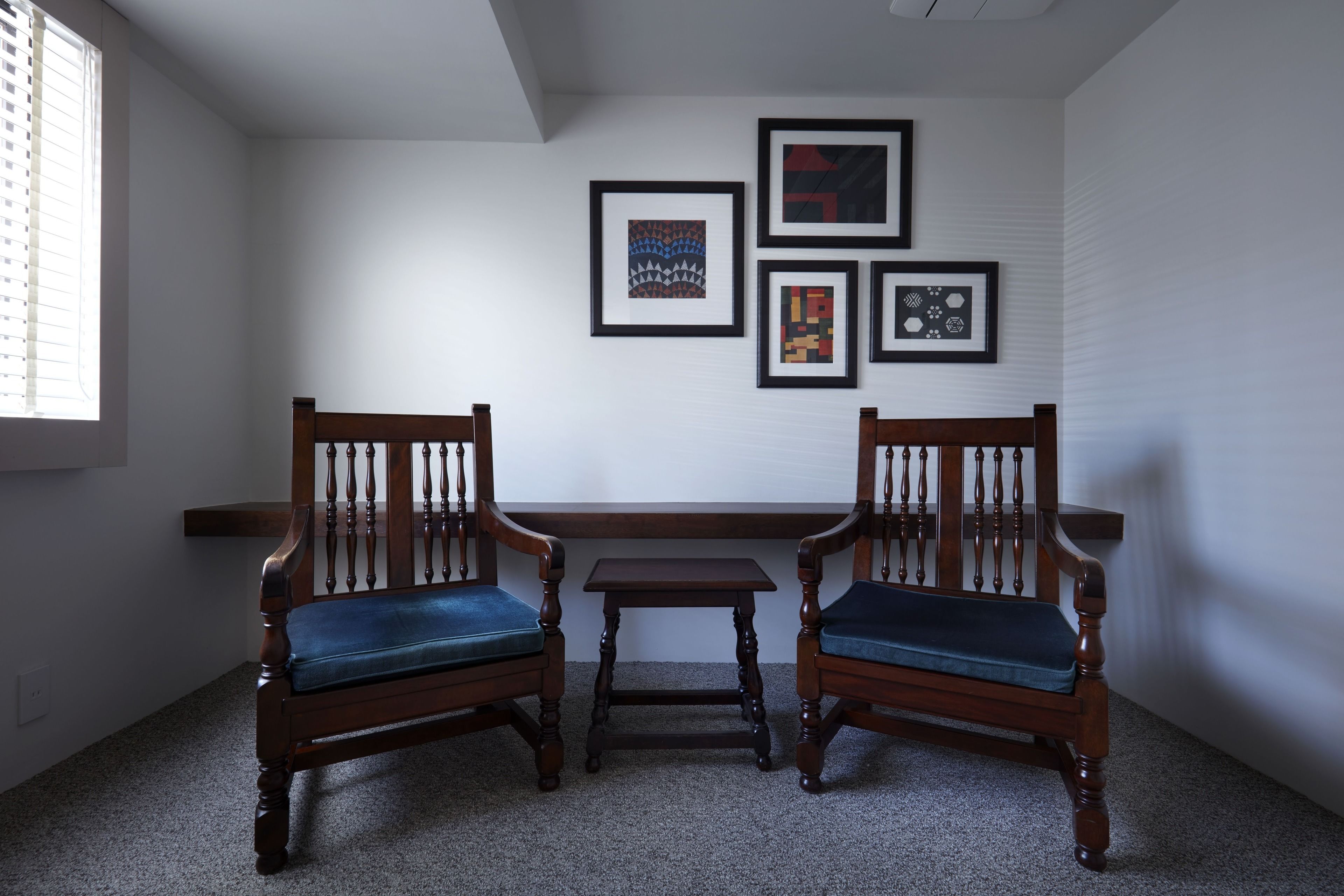 Ein Zimmer mit zwei Holzsesseln mit blauen Kissen, einem kleinen Holztisch und drei gerahmten Kunstwerken an der Wand.
