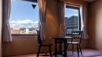 Una habitación con una mesa de comedor y sillas, ventanas grandes con cortinas y vistas a edificios y montañas.