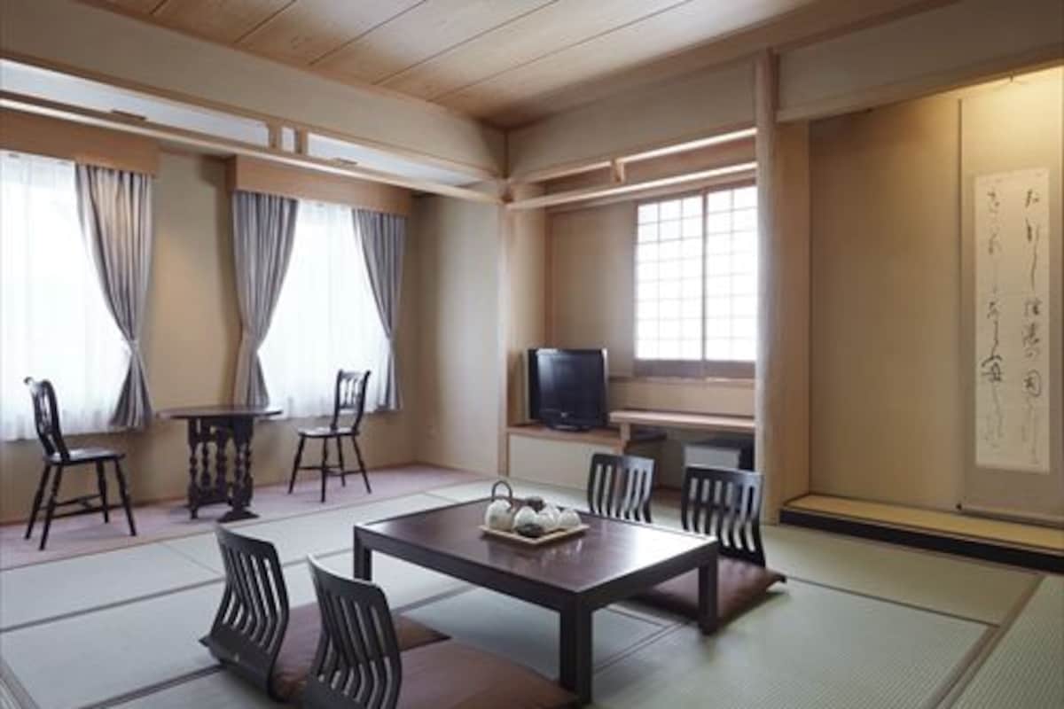 A traditional Japanese-style room with tatami flooring, a low table with cushions, and a television on a stand.