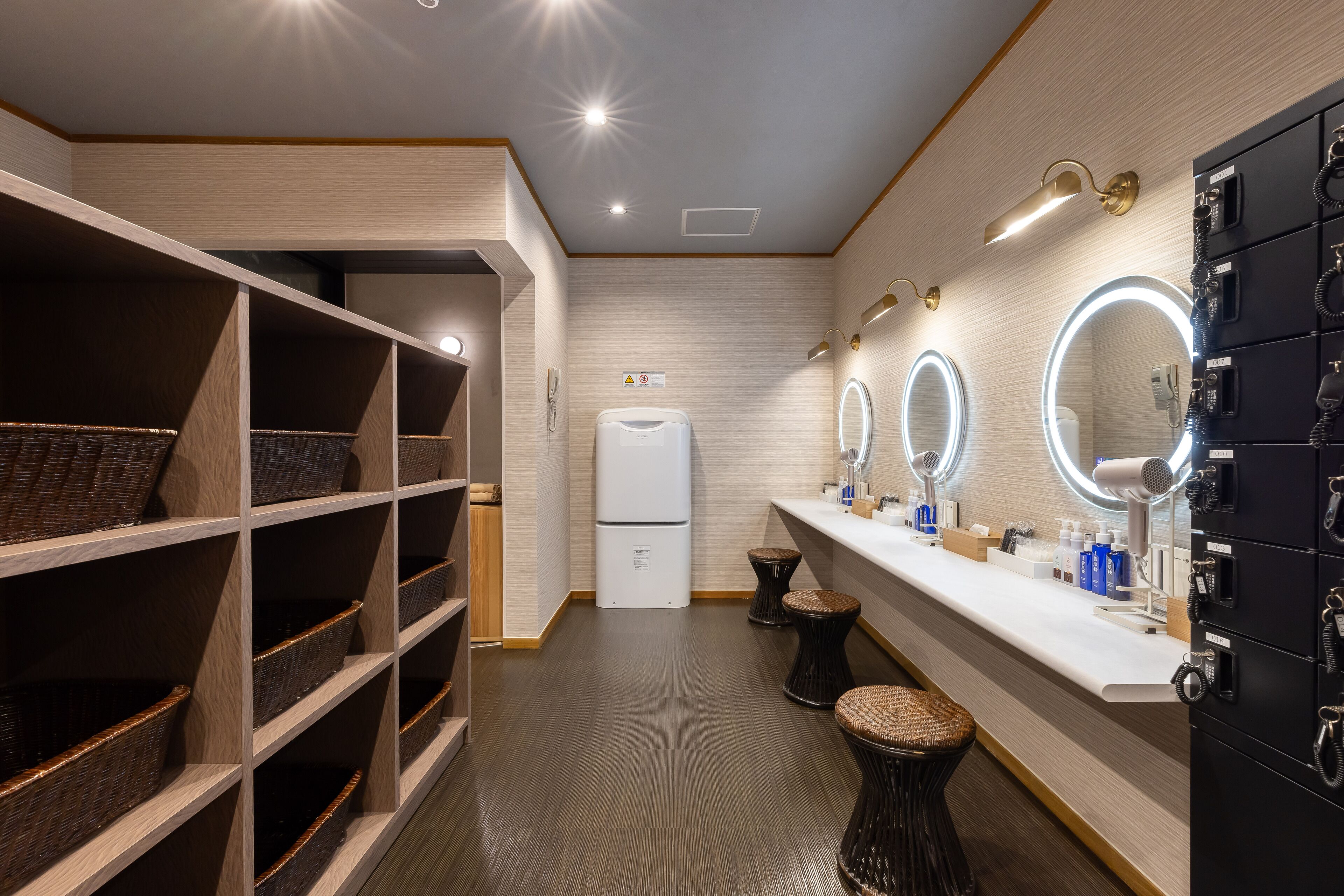 Une salle de bain moderne avec un meuble-lavabo, trois miroirs, un réfrigérateur et des paniers en osier placés sur des étagères.