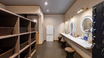 A modern bathroom with a vanity, three mirrors, a refrigerator, and wicker baskets on shelves.
