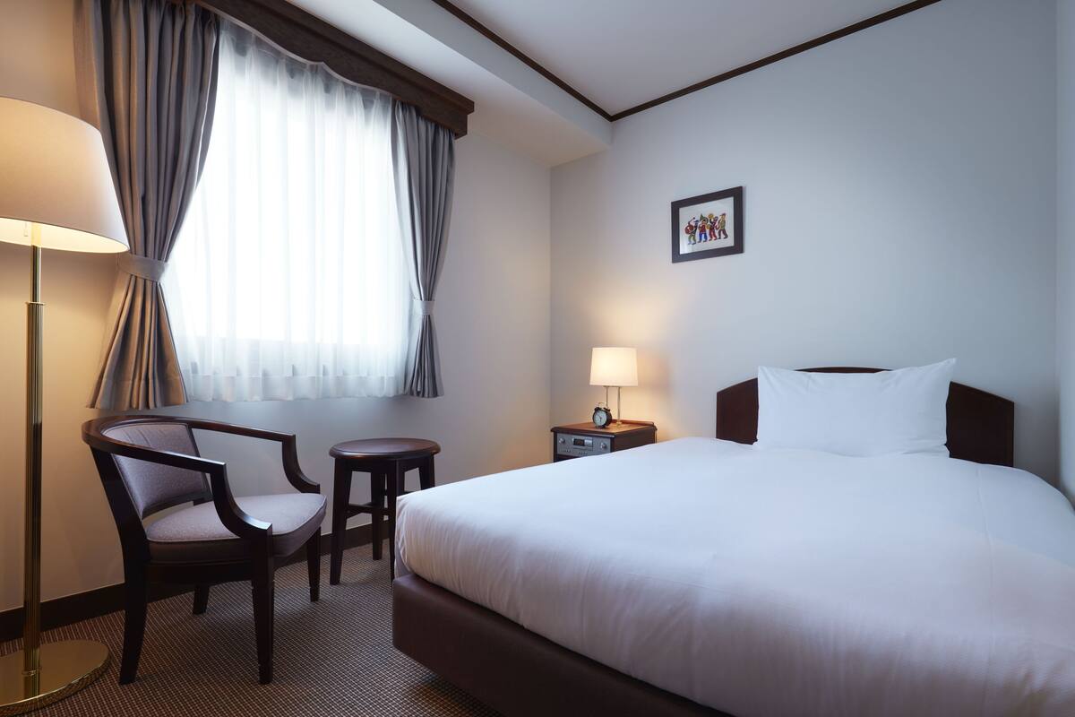 A hotel room with a large bed, a desk with a chair, a lamp, and a picture on the wall.