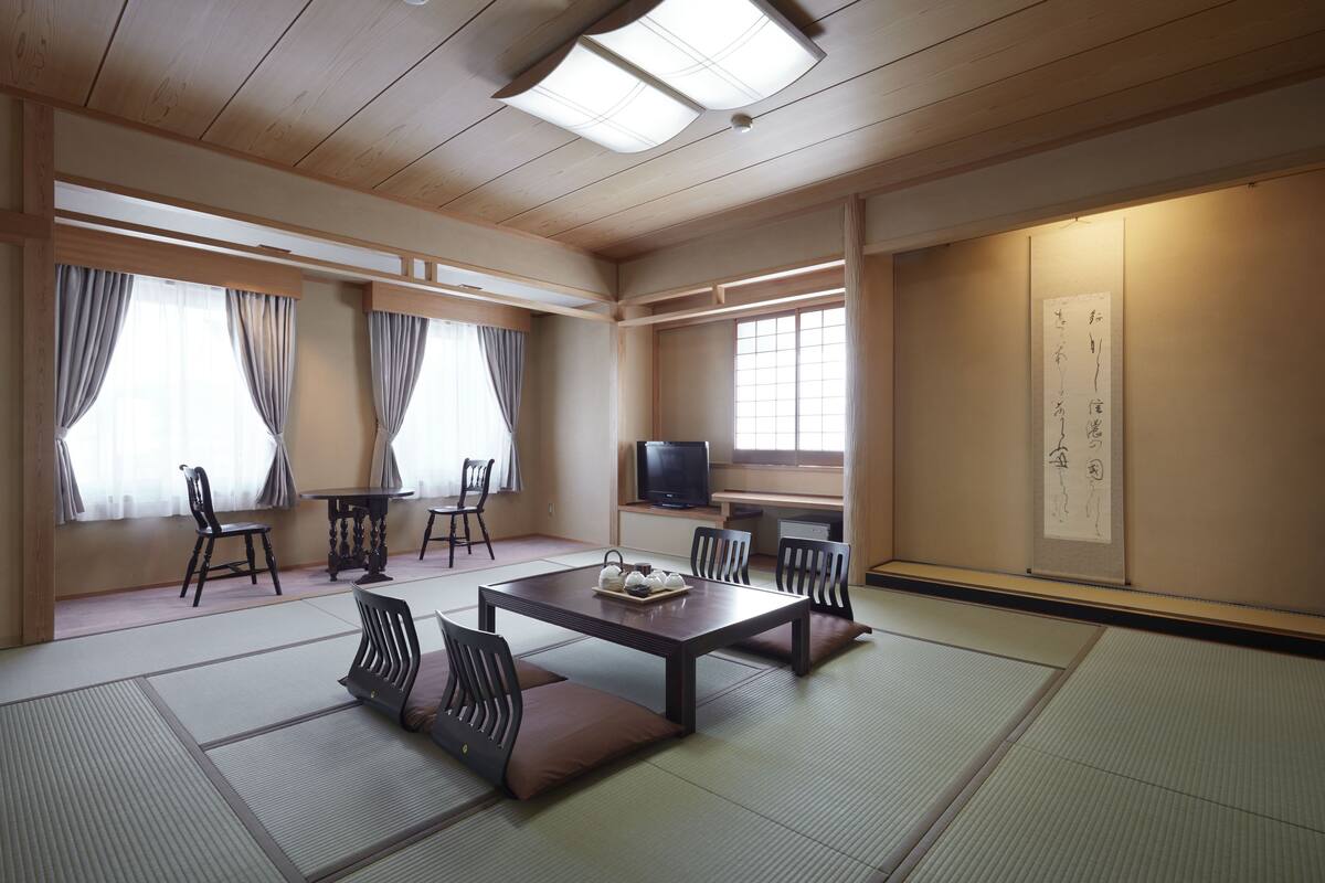 A traditional Japanese room with tatami flooring, a low table with cushions, and a television.