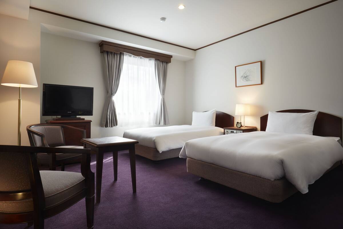 A hotel room with two beds, a TV, a desk, and a chair.