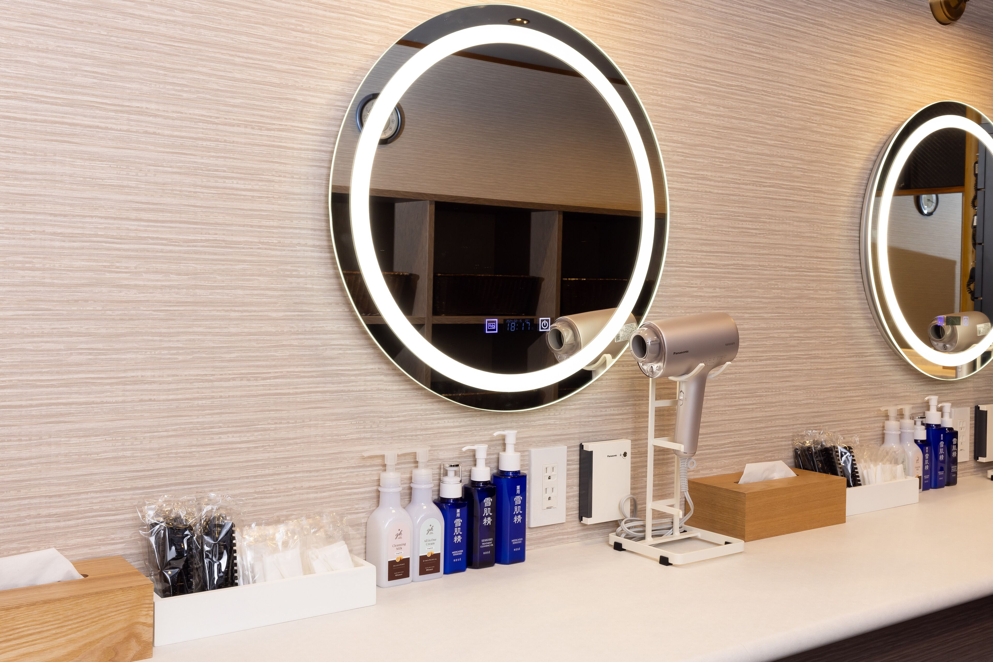 A bathroom with a round mirror, a hairdryer, and various toiletries on the counter.