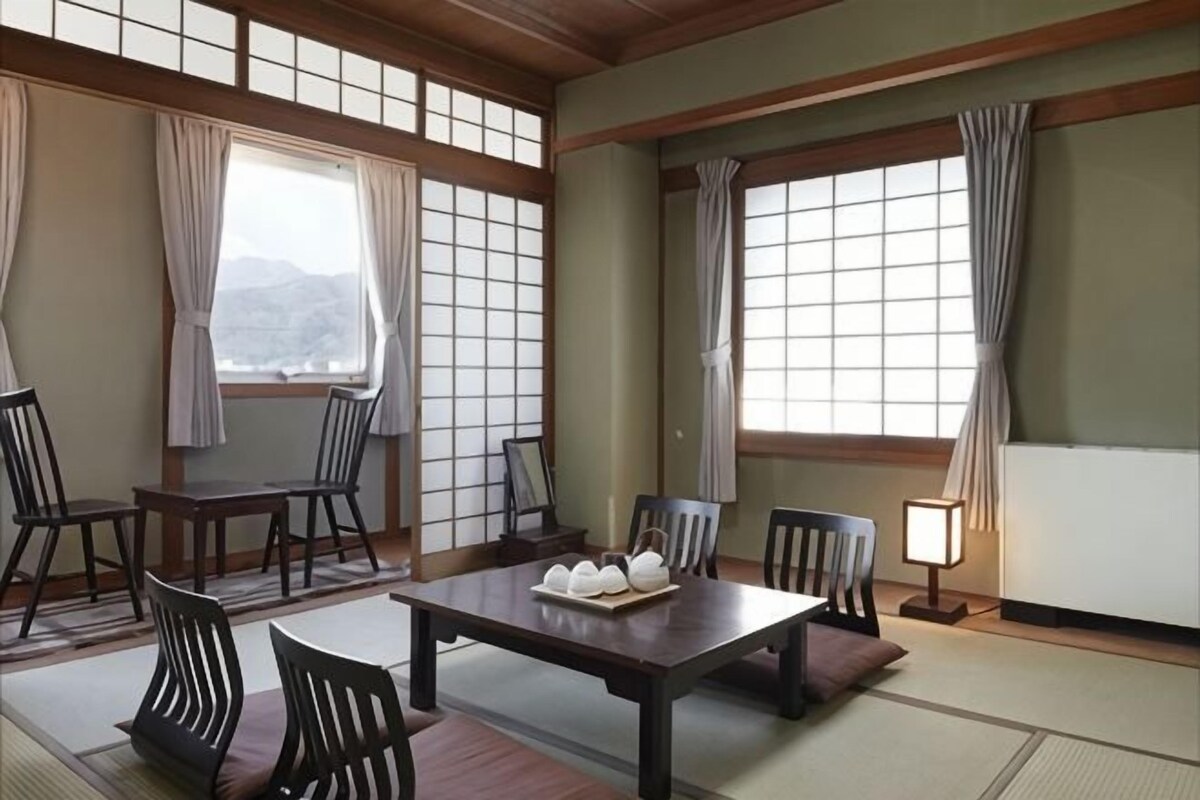 A traditional Japanese room with tatami flooring, a low table with a tray of white items, and wooden furniture.