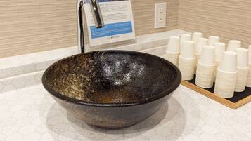 A large ceramic bowl sink with a faucet, a stack of white paper cups, and a sign with text and images.