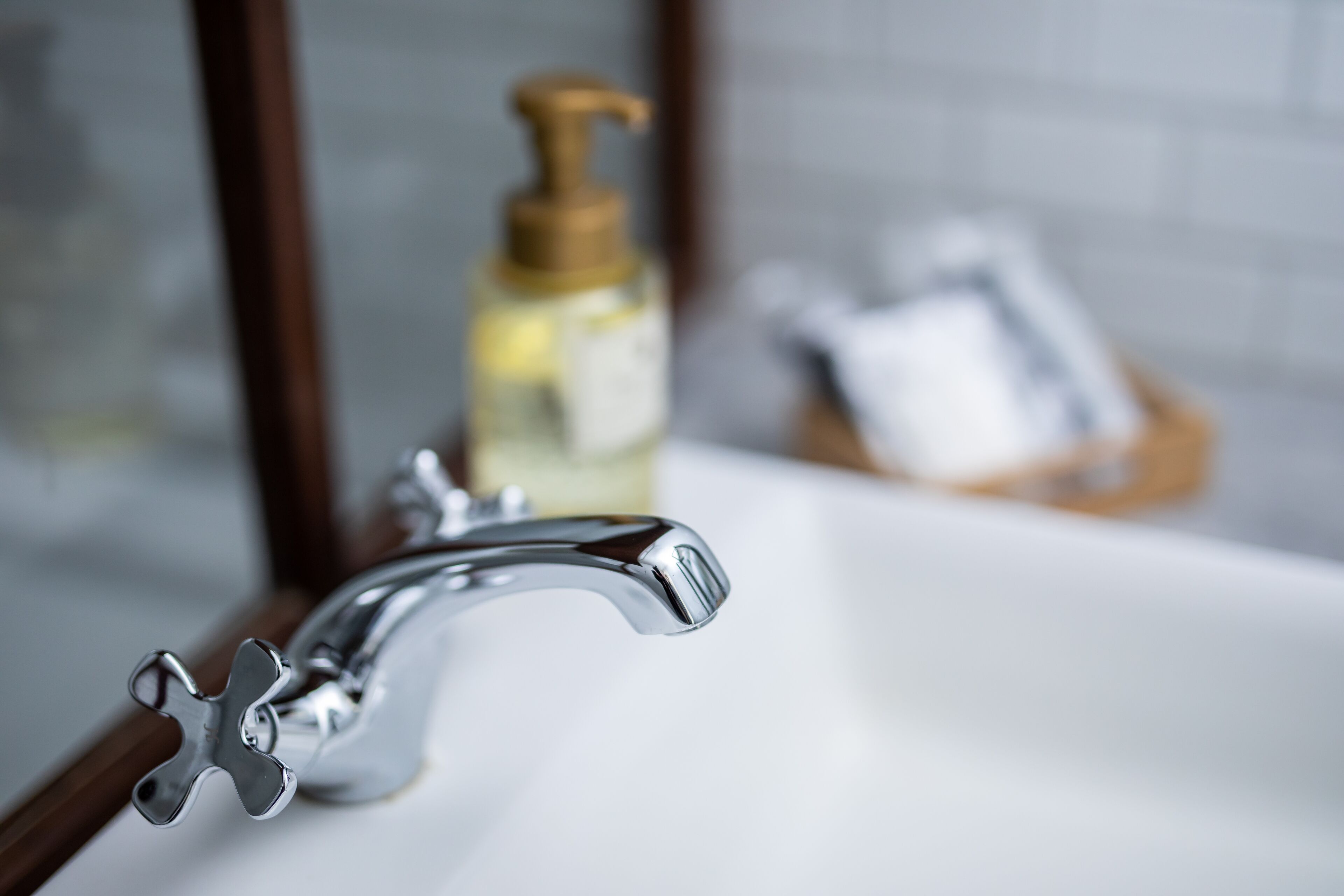 A bathroom sink with a chrome faucet and a soap dispenser in the background.