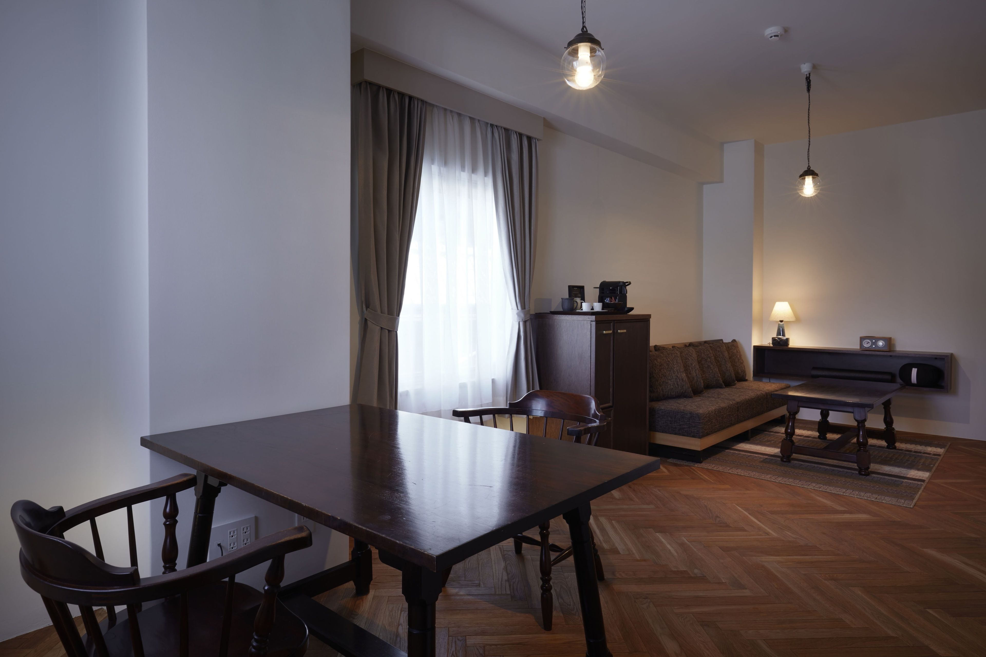 Un salon moderne avec une table à manger en bois, un canapé et une table basse. On y trouve une fenêtre avec des rideaux, un luminaire au plafond et une étagère murale avec une lampe.