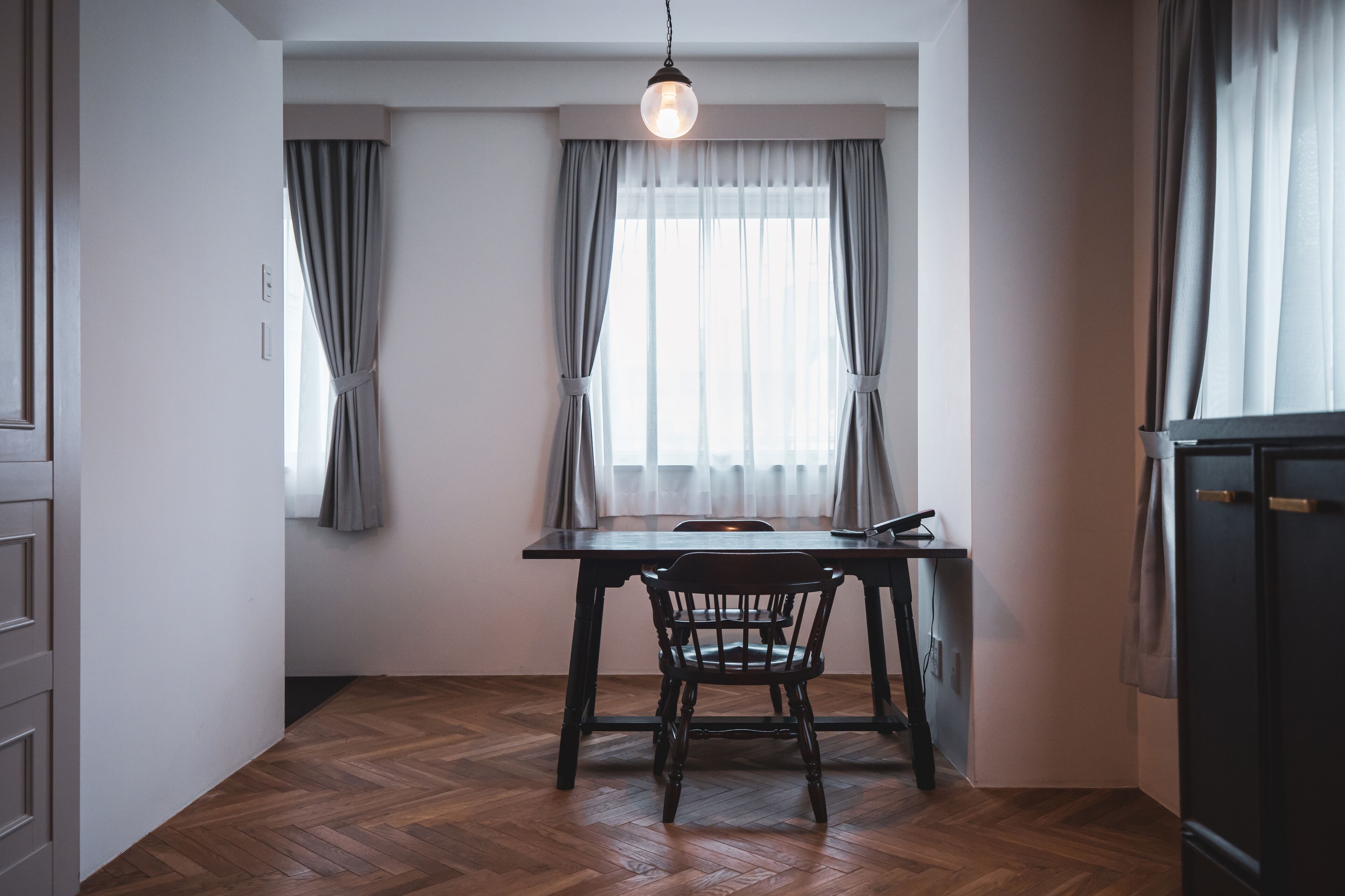 Un petit coin repas avec une table et des chaises en bois, un luminaire suspendu et une fenêtre avec des rideaux.