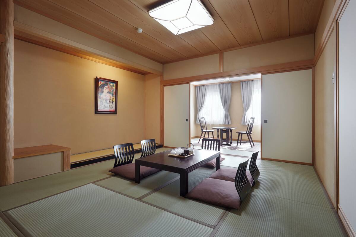 A traditional Japanese room with tatami flooring, a low table with cushions, and a sliding door leading to a dining area.