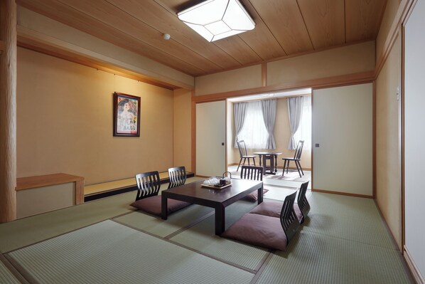 Una habitación japonesa tradicional con suelo de tatami, una mesa baja con cojines y una puerta corredera que da a un comedor.